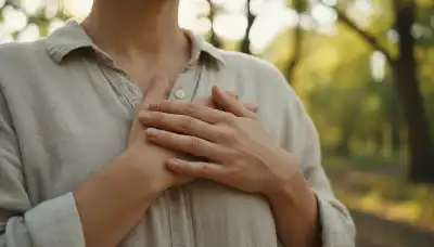 A close-up photorealistic image of a person's hands gently resting over their heart center. The hands look warm, grounded, and relaxed. The background is softly blurred, showing elements of a calm natural setting like green leaves and soft sunlight filtering through trees. Deeply emotional, serene, sharp focus on the hands and chest.
