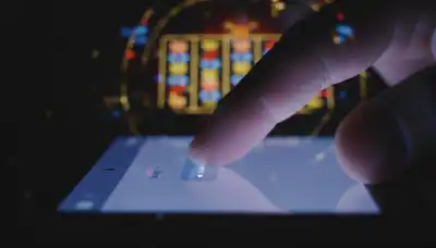 A photorealistic, highly detailed macro shot of a thumb hovering anxiously over a smartphone screen displaying a chat interface. The screen emits a faint neon glow in a darkened room. Subtly blended in the background through a double-exposure effect are blurred, glowing lights of a casino slot machine. Intense emotional atmosphere, dramatic lighting, portraying digital addiction and the anticipation of a digital reward.