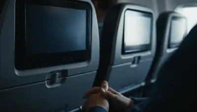 Hyper-realistic close-up of a blank, turned-off airplane seatback screen. In the gently blurred foreground, a passenger's hands rest perfectly still on their lap. Soft blue cabin light reflecting off the dark screen, symbolizing total digital disconnect and an escape from entertainment. 85mm lens, shallow depth of field, 4k.