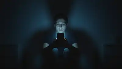 Photorealistic image of a person sitting alone in a completely dark, shadowy room, holding a smartphone close to their face. The cold, harsh blue light from the screen starkly illuminates their features, revealing a stressed, wide-eyed, and overwhelmed expression as they relentlessly scroll. High contrast, modern digital age aesthetic, moody lighting.