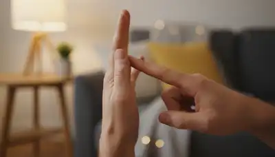 A highly detailed, photorealistic macro shot of a person's hand gently tapping the side of their other hand (the 'karate chop' point). The background is beautifully blurred (bokeh) showing a cozy, softly lit living space. Warm, comforting lighting. Skin texture is highly realistic, conveying a sense of somatic grounding and safety.