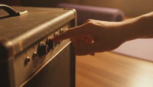 Fotografía de detalle (close-up) fotorrealista: Una mano en primer plano presionando con firmeza el botón de 'Play' en un amplificador de guitarra vintage de textura rugosa. En el fondo, profundamente desenfocado pero reconocible, hay una esterilla de yoga morada enrollada y abandonada en el suelo de madera. Iluminación cálida, polvo flotando en el ambiente.