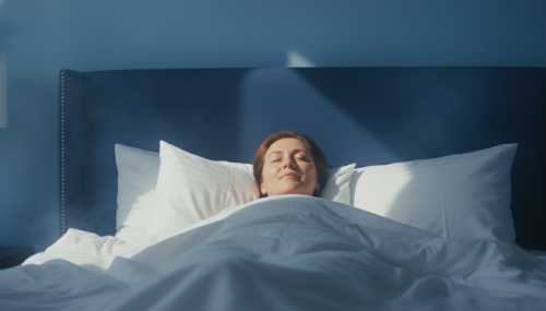 Conceptual yet photorealistic image of a person sleeping peacefully in a comfortable bed. A subtle, warm golden lighting bathes their face, representing a deep state of relaxation and the flow of Alpha brainwaves. Deep blue background with soft, soothing tones, serene mood, high-quality editorial photography.