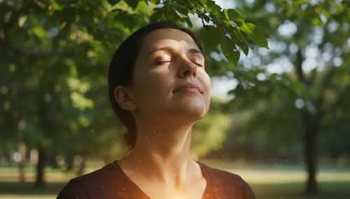 A photorealistic portrait of a person taking a deep, calm breath outdoors, soft and warm sunlight filtering through green tree leaves. Subtle, glowing cinematic light represents a sense of sudden mental clarity and biological reset. High detail, shallow depth of field, 8k resolution, conveying inner peace and grounding.