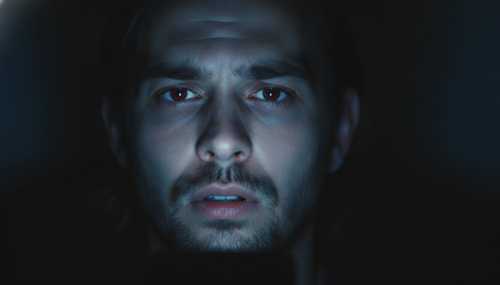 Fotografía hiperrealista, primer plano del rostro de una persona iluminado únicamente por el brillo de la pantalla de un smartphone en la oscuridad. Su expresión denota agotamiento profundo y sobrecarga mental, ojos cansados. Iluminación cinematográfica, alta calidad 8k, estilo documental.