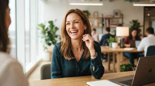 A confident and radiant 43-year-old woman with subtle laugh lines laughing with genuine joy. The background is a clean, modern workspace with soft natural sunlight streaming through a window. The focus is sharp on her expression, capturing emotional clarity and vitality. Editorial photography style, warm tones, high-resolution.